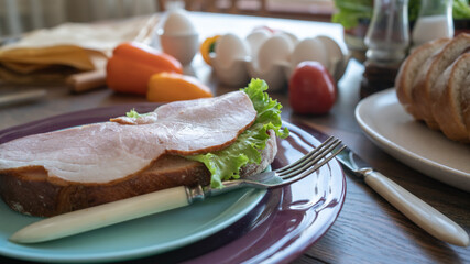 Sandwich with ham and green salad on a plate. Kitchen table. Breakfast. Close-up. Soft focus in the background