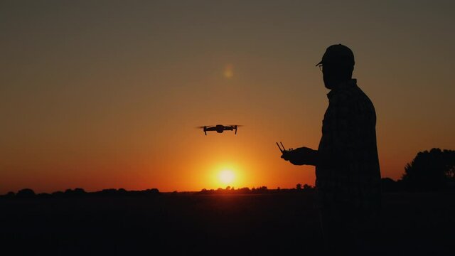 Silhouette of a man controls a drone at sunset directing its flight towards the sun