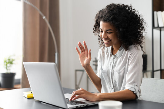 Young African American foreign language tutor starting the on-line lesson with trainee, waving, smiling at the laptop screen. Mixed-race woman typing an email, multitasking, e-learning process concept