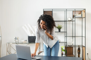 Busy multitasking young African American sales representative on a phone call at the home office,...