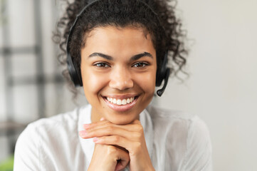 Headshot of friendly African American millennial woman in a headset sitting with her hands on a...