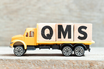 Fototapeta premium Toy truck hold alphabet letter block in word QMS (abbreviation of quality management system) on wood background