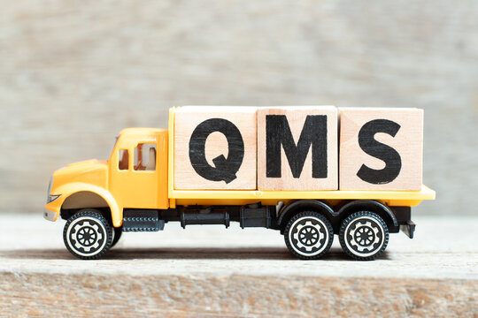 Toy truck hold alphabet letter block in word QMS (abbreviation of quality management system) on wood background