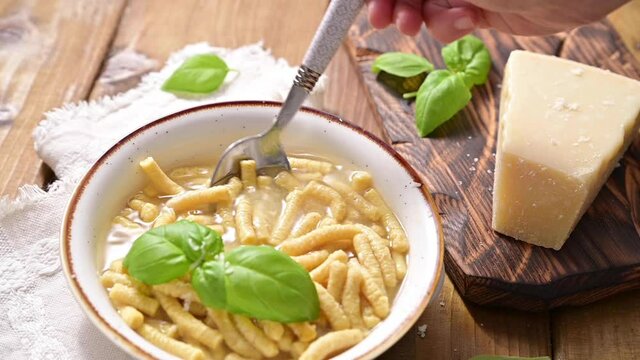 Passatelli in broth - pasta cooked in chicken broth. Hand takes the pasta with a spoon. A pasta formed of bread crumbs, eggs, grated Parmesan cheese. Typical for Pesaro, Urbino and Emilia Romagna. 