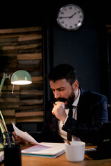 Exhausted businessman working on computer in the office. Tired man sitting at office desk drinking coffee..