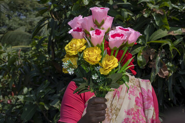 Selective focus shot of a female in a pink sari holding a colorful artificial flower bouquet