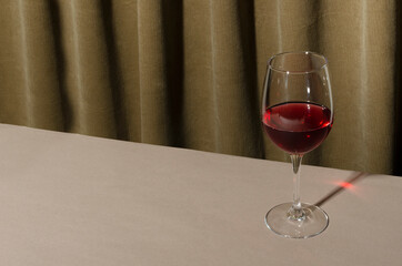 Closeup of one glass of red wine on the table against folds of curtains.Empty space.Hard light