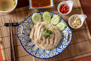 Closed up Chinese chicken rice that serve soup and spicy source, on wooden table and chopsticks, traditional Hainanese food