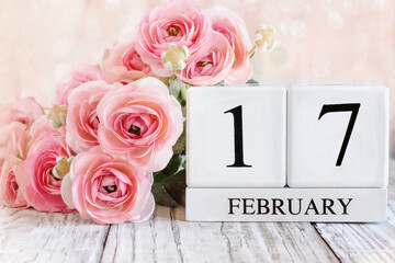 White wood calendar blocks with the date February 9th and pink ranunculus flowers over a wooden...