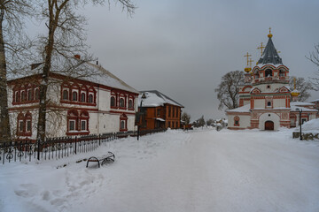 Winter cityscape with a majestic old church, the historic governor's house, a bench in the snow and tall trees. Center of the city of Solikamsk (Northern Ural, Russia) in a winter cloudy day 