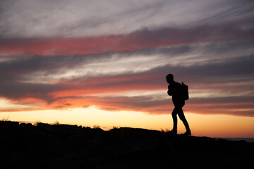 Silhouette of a male traveller with a backpack climbing up the mountain against beautiful sky
