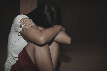 Young woman sitting on floor with arm around lower head in dark room, sexual violence , sexual abuse, human trafficking concept