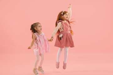 Jumping. Childhood and dream about big and famous future. Pretty little girls on coral pink studio background. Childhood, dreams, imagination, education, facial expression, emotions concept.
