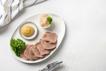 Sliced beef tongue, classic serving with mustard and horseradish sauce for choice on white table. View from above.