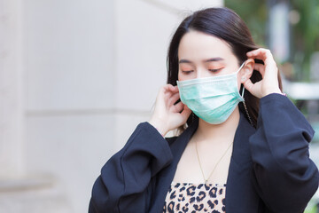 Beautiful Asian girl in black coat is wearing a medical face mask to protect respiratory system from Coronavirus-19 (COVID-19) infection.