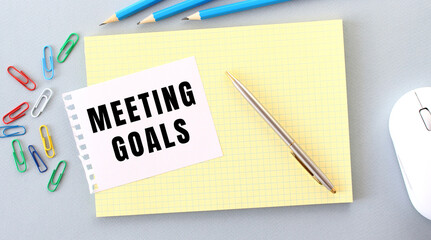 MEETING GOALS is written on a piece of paper that lies on a notebook next to office supplies.