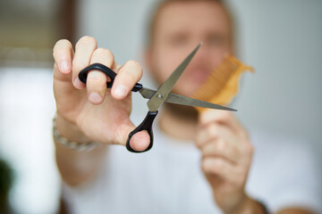 A male hairdresser wih bread holds scissors and a comb in his hands, barbershop