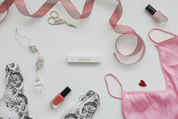 Concept Women's Day, March 8. Female underwear with a red ribbon and cosmetics on white background. Styled flat lay, top view, copy space. 