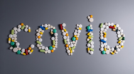 Sign COVID made of pills, tablets and capsules on gray table