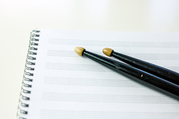 Drum sticks of black color on a music notebook on a white table, top view. Hobby music concept, art background, copy space