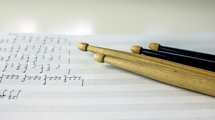 Two wooden drumsticks of light color on a music book on a white table, top view. Hobby music concept, art background, copy space, close-up