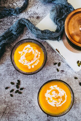 Soupe de courge au curry et baies roses dans un bol sur un fond couleur béton