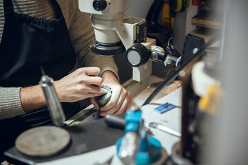 Craftsman. Close up hands of jeweller, goldsmiths making of golden ring with gemstone using professional tools. Craft production, precious and luxury jewel, hand made occupation. Workshop, artwork.