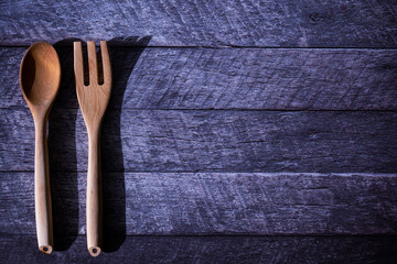 A couple of wooden utensil, a spoon and a carving fork, laid on a dark wooden table with copy space on the right side