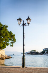 Obraz premium Single street lamp on the pier seafront with flowing water at sunset.
