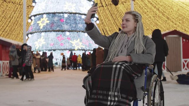 Young woman in a wheelchair at Christmas party on the streets - taking a photo and fixes her dreadlocks