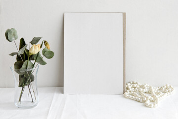 Fashion wedding stationery mockup scene. An empty vertical greeting card and dried white flowers on a white linen background. Feminine still life, top view.