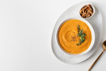 Pumpkin soup served crackers and microgreens isolated on white table. View from above.