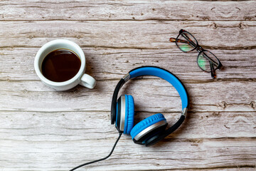 A pair over over ear wired headphones laid on a wooden table or desk next to a coffee and a pair of glasses