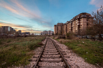 Fototapeta na wymiar urban Industrial landscape at dusk, in a sunset evening, in Belgrade, Serbia, with a single railway track passing in the middle of industries while the chimney of a factory can be seen in background.