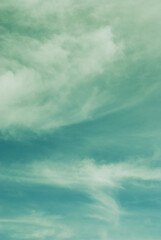 Fototapeta premium Colorful blue green sky with dramatic soft light clouds. Vertical capture natural image background.