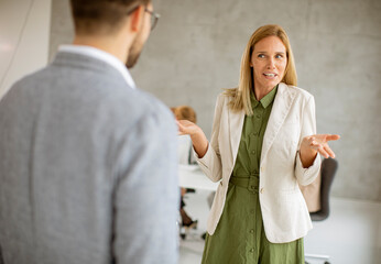 Man and woman business couple discussing indoors in the office with young people works behind them