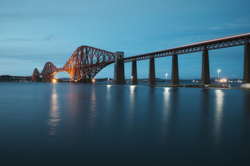 Obraz premium View of Forth Rail Bridge at night and and the glow trail of a moving train over the sea. View of Forth Rail Bridge, the worlds longest cantilever bridge, Scotland, United Kingdom