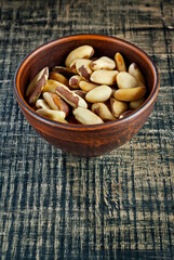Brazil nuts in a clay bowl on a wooden table. Nuts on a black shabby board. Copy space and free space for text near nuts.