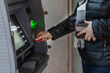 Female hands hold a plastic bank credit card, use an ATM machine to withdraw money.