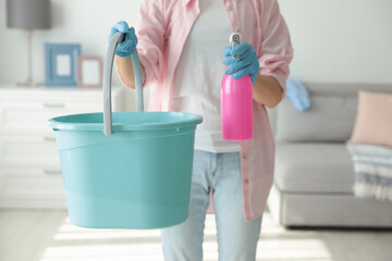 Woman holding bucket and bottle of cleaning product at home, closeup