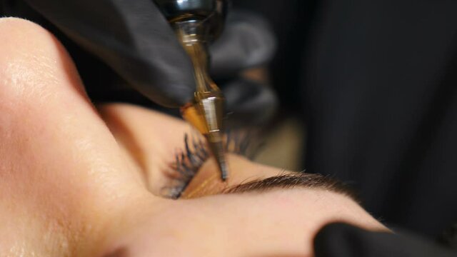 Microblading eyebrow tattoo, permanent makeup. Beautician in gloves, using special needle, injects pigment into skin and stains eyebrows. Cosmetologist applying permanent make up on eyebrows. 4 k
