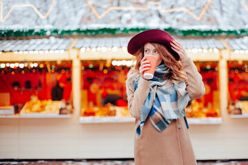 beautiful young woman in a felt hat and coat walking in the romantic city and drinking her coffee. street food at fair   