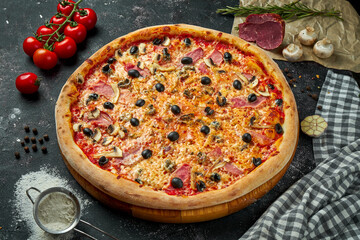 Appetizing italian pizza with cheese, ham, mushrooms, olives and red sauce in a composition with ingredients on a black background