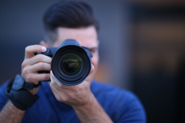 Photographer taking picture with professional camera outdoors in evening, focus on lens