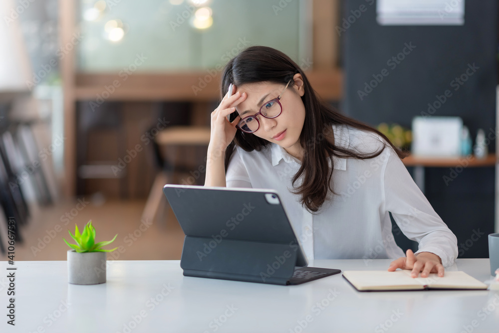 Wall mural Image of an Asian woman who is tired and overthinking from working with a tablet at the office.