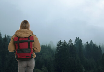 Tourist with travel backpack enjoying foggy mountain forest during vacation trip