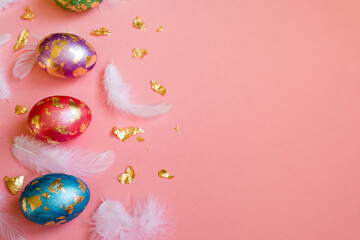 Fototapeta na wymiar Painted Easter eggs with golden foil on it, white feathers on the pink background.