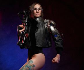 Obraz na płótnie Canvas Female warrior in cyberpunk style poses in dark background. Seductive and slim woman with glasses and cybernetic hand dressed in black jacket.