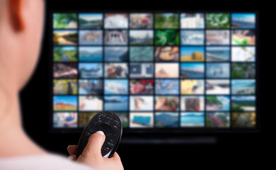 Online Multimedia video concept on TV set in dark room. Woman watching online TV with remote control in hand. VOD service screen. TV screen with lot of pictures