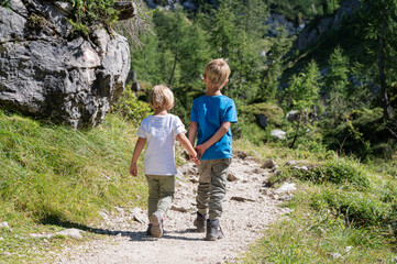 Rear view of two siblings holding hands while hiking on a trail